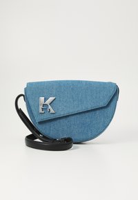Borsa a tracolla in denim blu con una forma curva, tracolla nera e accento del logo argentato. Tessuto morbido con chiusura a patta.