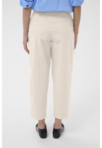Pantalons beiges raccourcis avec une coupe décontractée, dotés de deux poches arrière et d'une texture lisse. Portés avec des chaussures noires à enfiler, vue arrière présentée.
