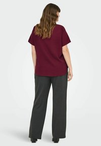 Burgundy kortärmad t-shirt med avslappnad passform, tillsammans med lösa grå byxor. Mjuk textur, rundad nederkant och minimal design.