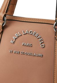 Tan nylon handbag featuring silver embossed branding: "KARL LAGERFELD PARIS" and "21 RUE ST-GUILLAUME." Hardware accents and textured surface.