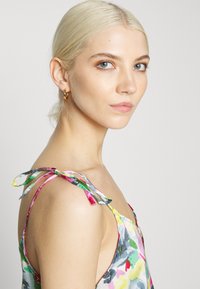 Vestido colorido com padrões florais, alças finas com detalhes de laço e um tecido suave e leve. Modelo exibe a peça de lado.