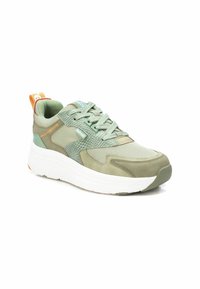 Zapatilla deportiva verde con materiales de malla y ante. Presenta una suela blanca gruesa, paneles texturizados y acentos en naranja contrastante.