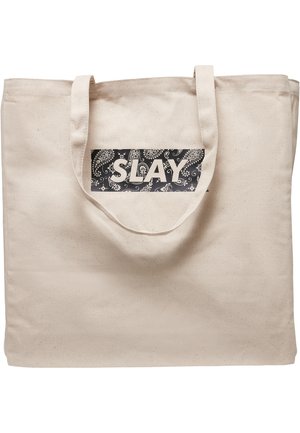 Canvas-Tragetasche in natürlichem Beige mit einem schwarzen rechteckigen Aufnäher, der den weißen Text "SLAY" und einen Paisleymuster-Hintergrund zeigt.