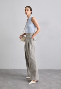 Light blue ribbed sleeveless polo top, gray pleated trousers, and pointed toe beige heels; features a small, structured beige bag.