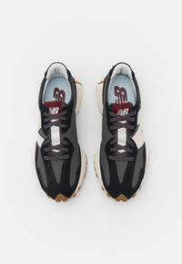Paire de baskets New Balance noires, grises et blanches avec logo bordeaux sur la languette et semelles en caoutchouc marron, vues de dessus sur fond blanc.