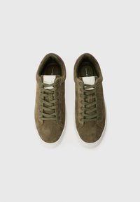 Olive green suede sneakers with a white rubber sole, featuring green laces, brown accents at the heel, and a tan logo patch on the tongue.