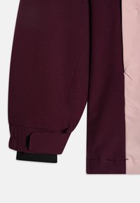 Burgunderfarbener Jackenarm mit elastischem schwarzen Bündchen, gewebte Stofftextur, mit kontrastierender pinker Innenauskleidung und Klettverschluss.