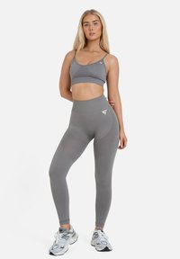 Senza maniche grigia sportiva e leggings a vita alta in tessuto testurizzato con dettaglio del logo, abbinati a scarpe sportive grigie.