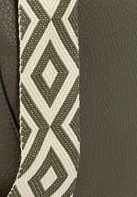 Bolso de cuero con una superficie verde oscura y una correa trenzada con un patrón de diamantes en crema y verde oliva. Materiales texturizados y duraderos.