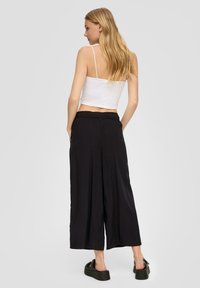 Zwarte wijde broek met een elastische tailleband, gecombineerd met een getailleerde witte crop top. Het materiaal lijkt soepel en licht van gewicht.