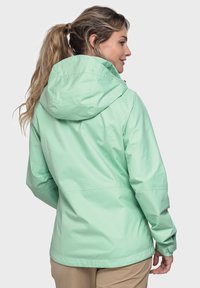 Mintgrüne wasserfeste Jacke mit Kapuze, die eine glatte Textur, ein schlankes Design und verstellbare Bündchen aufweist. Die Rückansicht zeigt die Nähte.