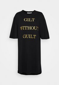 Černé tričkové šaty s krátkými rukávy, na kterých je zlatě vyšitý nápis "GILT WITHOUT GUILT." Hladký materiál, uvolněný střih a zakřivený lem.