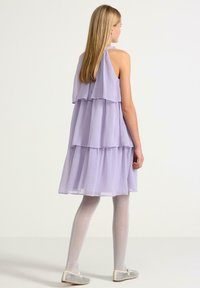 Fialové šaty s vrstvenými sukni s lehkým, průhledným materiálem. Mají horní část na krku a vrstvené volány, které splývají od ramen až po lem.