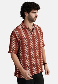 Camisa de manga corta con cuello en un patrón de zigzag rojo y blanco. La tela es texturizada, con un ajuste holgado y mangas enrolladas.
