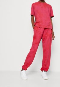 Pink tie-dye bomulds t-shirt og matchende joggers med elastiske manchetter, med et lille logo på bukserne. Styling med hvide sneakers.