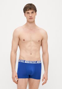 Sinised puuvillased bokserpüksid valge logodega elastse vöökohaga, mis istuvad tihedalt ja millel on sile tekstuur. Ilma mustriteta, minimalistlik disain.