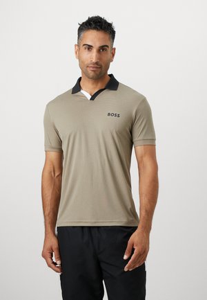 Beige Poloshirt mit einem schwarzen Kragen und weißen Akzenten. Aus dünnem, strukturiertem Stoff gefertigt und mit einem kleinen schwarzen "BOSS"-Logo auf der Brust.