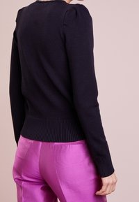 Navy knitted sweater with a ribbed hem and puffed sleeves, paired with bright pink satin pants, showcasing smooth textures.