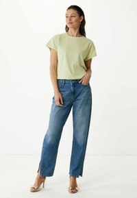 Jasnozielona bawełniana koszulka z podwiniętymi rękawami, w połączeniu z niebieskimi jeansami o wysokim stanie z bokami rozciętymi do kostek. Proste sandały na obcasie.