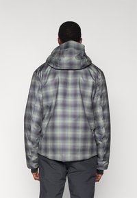 Chaqueta con capucha, presenta un patrón de cuadros en tonos verdes, morados y grises. El material es suave y tiene un ajuste relajado.