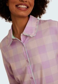 Ljuslila och krämfärgad rutig skjorta med volangkrage och turkos kant; har knappar och en mjuk textilstruktur.