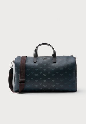 Tmavě modrý válcový cestovní vak s černými úchyty a hnědým nastavitelným ramenním popruhem s jemným opakujícím se vzorem loga.