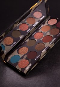 Tarnmuster-Lidschattenpalette mit 12 Nuancen, darunter Brauntöne, tiefes Blau und Kupfer; matte und schimmernde Finishes.