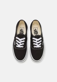 Black canvas sneakers with white laces, padded collar, and white rubber sole. Features contrast stitching and Vans logo on the insole.