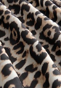 Tissu en imprimé léopard présentant un fond beige avec des motifs tachetés noirs et bruns. La texture semble tissée et légèrement transparente.