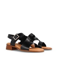 Sandal de cuero negro con correas cruzadas, hebilla ajustable y un tacón bajo apilado. Plantilla color tostado y textura suave con un diseño minimalista.