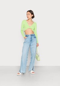Suéter cropped verde canelado, jeans retos azul claro com fendas laterais, sandálias de plataforma brancas e uma pequena bolsa verde clara.