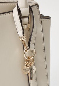 Borsa beige in materiale sintetico liscio, con hardware color oro, doppie decorazioni a forma di cuore e bordature scure a contrasto lungo i lati.