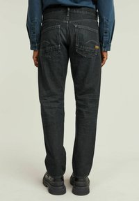 Tumedat denim püksid sirge lõikega, tagakottide ja kontrastsete õmblustega. Kandmisel mustade saabaste ja sinise särgiga.