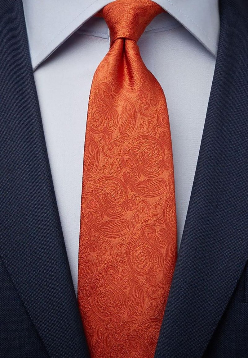 Orange paisley slipslips för gjort av slät tyg, med en upphöjd textur. Bärs över en ljusblå skjorta och en mörk marinblå kavaj.