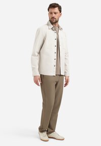 Lichtbeige jas met knopen aan de voorkant, twee borstzakken en puntkraag, gecombineerd met taupe broek en beige sneakers. Eenvoudig en modern ontwerp.