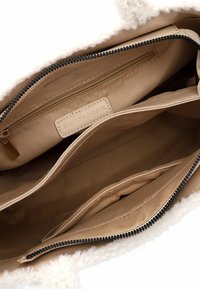 Interno di una borsa beige con fodera in peluche crema, dotato di una tasca con zip e due scomparti aperti. L'etichetta riporta "EMILY & NOAH."