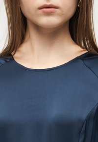 Κοντινό πλάνο του κάτω μέρους του προσώπου και του λαιμού ενός ατόμου που φοράει μπλε μπλούζα με στρογγυλή λαιμόκοψη και έχει μακριά, ίσια μαλλιά εμφανή.