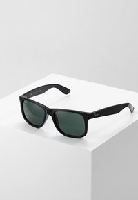 Ochelari de soare din plastic negru cu lentile de un verde închis, rame dreptunghiulare late și sigla Ray-Ban pe lateral. Textură netedă și design modern.