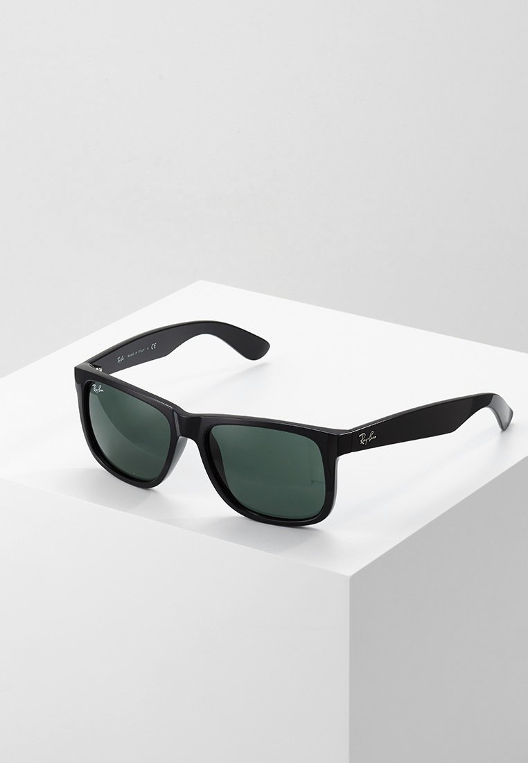 Ochelari de soare din plastic negru cu lentile de un verde închis, rame dreptunghiulare late și sigla Ray-Ban pe lateral. Textură netedă și design modern.