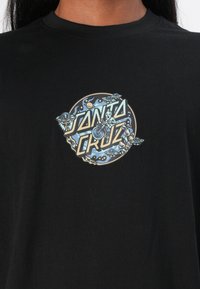 Zwarte katoenen t-shirt met een circulaire grafiek met de tekst "SANTA CRUZ", een ruimte-thema ontwerp en kleurrijke details van een skelet en UFO.