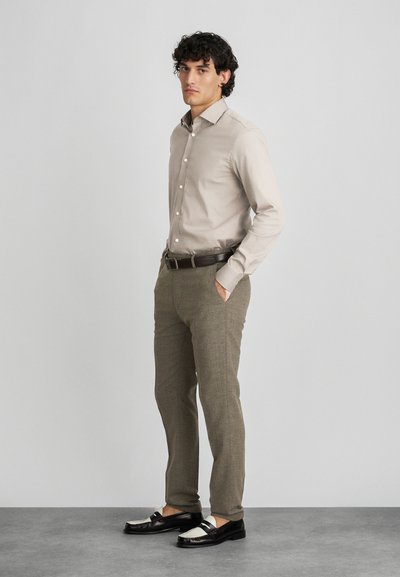 Beige button-up shirt, gray textured trousers, and two-tone shoes with a black and white design. Styled with a brown belt.