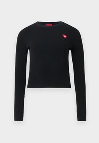 Top preto de manga comprida com padrão canelado, apresentando decote redondo e um pequeno remendo de coração vermelho no peito. Textura suave e design ajustado.