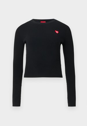Svart ribbet langermet topp med rund hals og en liten rød hjertepatch på brystet. Myk tekstur og tettsittende design.