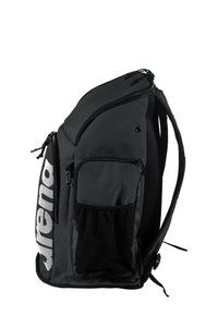 Sac à dos noir avec plusieurs compartiments zippés, poche latérale en maille et finition texturée. Comprend un grand logo blanc sur un côté.