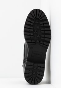 Semelle de chaussure noire avec une surface en caoutchouc texturé. Présente des motifs de crantage profonds pour l'adhérence et inclut le nom de la marque "ANNA FIELD." La taille 37 est visible.