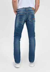 Vaqueros de denim azul de corte slim con un acabado ligeramente descolorido, que cuentan con dos bolsillos traseros y un parche de cuero marrón en la cinturilla.
