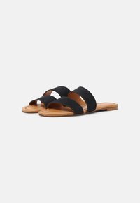 Sandali piatti con due ampie cinghie in suede nero e sottopiedi imbottiti color pelle su uno sfondo bianco.