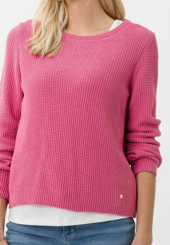 Maglione rosa lavorato a maglia con un motivo testurizzato, scollatura rotonda e polsini a coste. Sovrapposto a una camicia bianca, con un piccolo accento metallico.