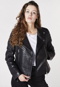 Svart lädermotorcykeljacka med vadderade axlar, silverfärgade dragkedjor, smal passform och en slät textur. Bärs över en vit skjorta.