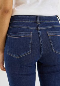 Vaqueros de mezclilla azul oscuro con una cintura de altura media, que cuentan con dos bolsillos traseros con detalles de costura y un acabado suave.